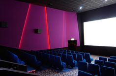 an empty auditorium with blue chairs and purple walls, while the screen is lit up