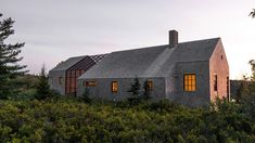 the house is surrounded by trees and bushes, with its windows lit up at night