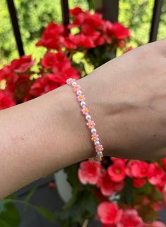 Glass bead bracelet with pink petals, yellow centers, and pearl beads. Pink Friendship Bracelets For Spring, Handmade Pink Pearl Bracelet, Spring Beaded White Pearl Bracelet, Dainty Pink Pearl Bracelets, Pink Flower Beaded Bracelets For Summer, Handmade Dainty Pink Pearl Bracelet, Spring Pink Beaded Bracelets With Colorful Beads, Dainty Pink Pearl Bracelet, Dainty Pink Beaded Pearl Bracelet