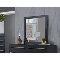 a large mirror sitting on top of a dresser next to a plant and vase in front of it