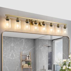 a bathroom with a large mirror and lights on the wall next to a shelf filled with flowers