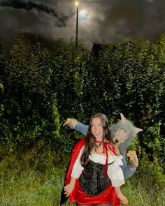 a woman dressed as a wizard carrying a baby in her arms while standing next to a hedge