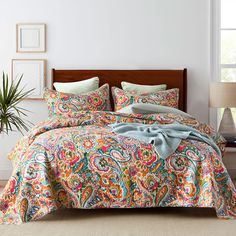 a bedroom with a bed covered in a colorful comforter and matching pillowcases