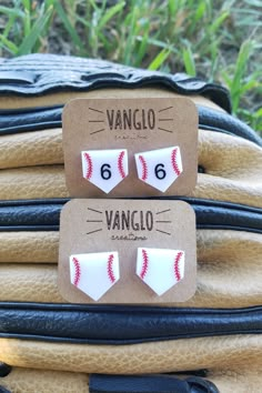 two pairs of earrings with baseballs on them are sitting on top of luggage in the grass