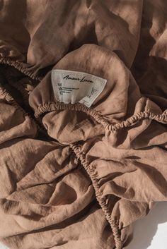 an unmade bed with a brown comforter on it's side and a tag hanging from the top