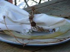 a white plate topped with a piece of cloth covered in beads and leaves next to a napkin on top of a wooden table