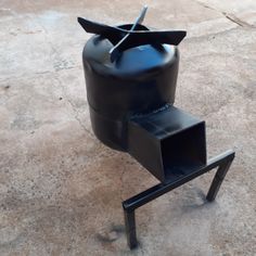 a black sculpture on top of a cement floor next to a metal stand with scissors sticking out of it