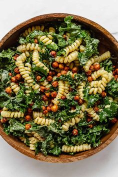 a wooden bowl filled with pasta and greens