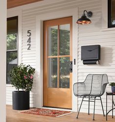 the front door of a house with two chairs and a potted plant