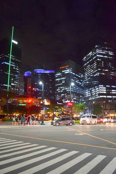 the city is lit up at night and people are crossing the street in the crosswalk