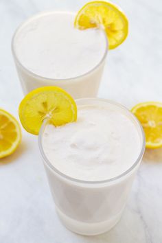 two glasses filled with white liquid and topped with lemons on a marble table top