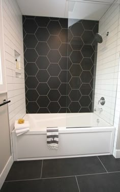 a white bath tub sitting next to a walk in shower under a black tiled wall