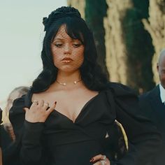 a woman in a black dress with her hands on her chest and other people behind her