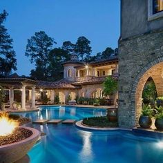 an outdoor swimming pool surrounded by stone pillars and arches with lights on each side at night