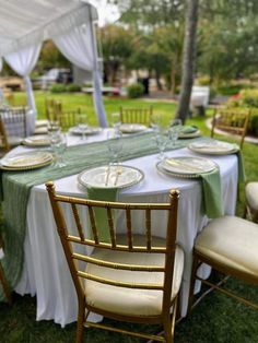 a table set up with white and green linens for an outdoor wedding reception in the grass