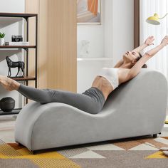 a woman laying on a grey couch with her legs up in the air while she's doing yoga