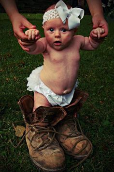 a baby in a diaper sitting on top of a pair of boots with her mother's hands