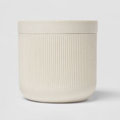 a white ceramic container with ribbed design on the front and bottom, sitting on a white surface