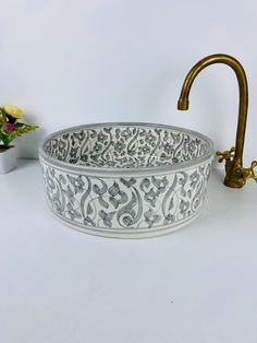 an ornate white and gold sink sits next to a vase with yellow flowers in it