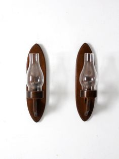 two wall lights mounted to the side of a white wall with wood and glass accents