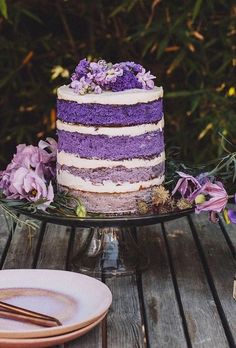 a purple cake sitting on top of a wooden table next to plates and silverware