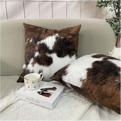 a cow print pillow sitting on top of a couch next to a cup and book