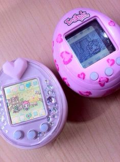 two electronic toys sitting next to each other on a wooden table, one pink and the other purple