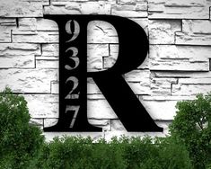 the letter r is shown in front of a white brick wall with trees and bushes