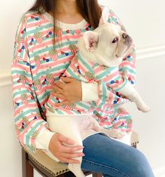 a woman sitting in a chair holding a small dog wearing pajamas on it's back