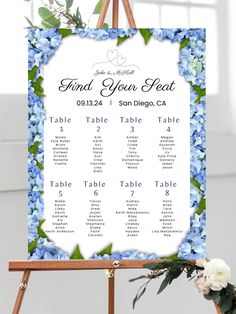 a blue floral wedding seating chart on an easel with flowers and greenery in the background