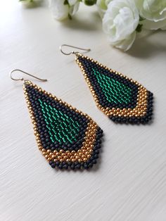 black and gold beaded earrings with green tears on a table next to flowers