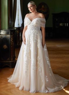 a woman in a white wedding dress standing on a wooden floor with her arms behind her back