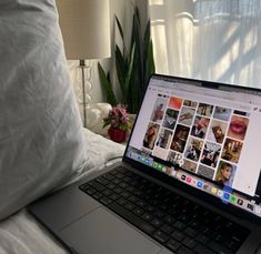 an open laptop computer sitting on top of a bed next to a lamp and pillows