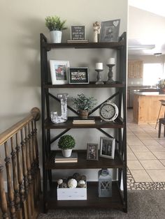 a bookshelf filled with pictures and plants on top of a wooden banister