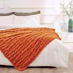 an orange blanket is on top of a white bed