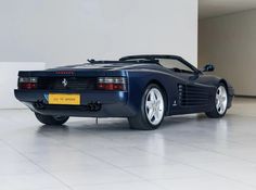 a blue sports car is parked in a room with white tile flooring and walls