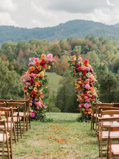 an outdoor ceremony set up with wooden chairs and flowers on the aisle, in front of mountains