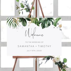 a welcome sign with greenery and white flowers on an easel in front of a window