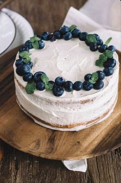 a cake with white frosting and blueberries on a wooden platter next to silverware