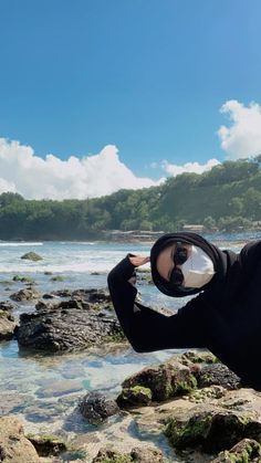 a man wearing a diving suit and goggles standing on rocks near the ocean