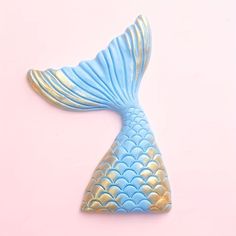 a blue and gold fish shaped object on a pink background