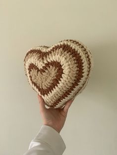 a hand holding up a crocheted heart shaped object in front of a white wall