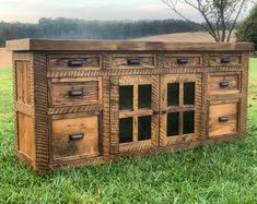 an old wooden cabinet sitting on top of a green grass covered field with trees in the background