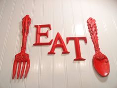 the word eat spelled with red plastic utensils on a white wall next to each other