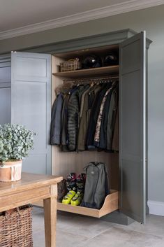 an open closet with clothes and shoes on the shelves next to a wooden table in front of it