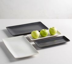 three black and white plates with green apples on one plate next to two smaller ones