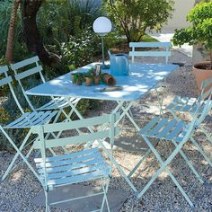 an outdoor table and chairs with potted plants on the gravel ground in front of a house