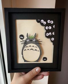 a person holding up a paper cut out of a totoro with eyes on it