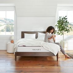 a woman is sitting on her bed looking at her cell phone while she sits in front of the mattress