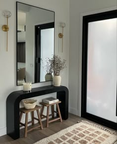 two stools sit in front of a mirror and table with vases on it